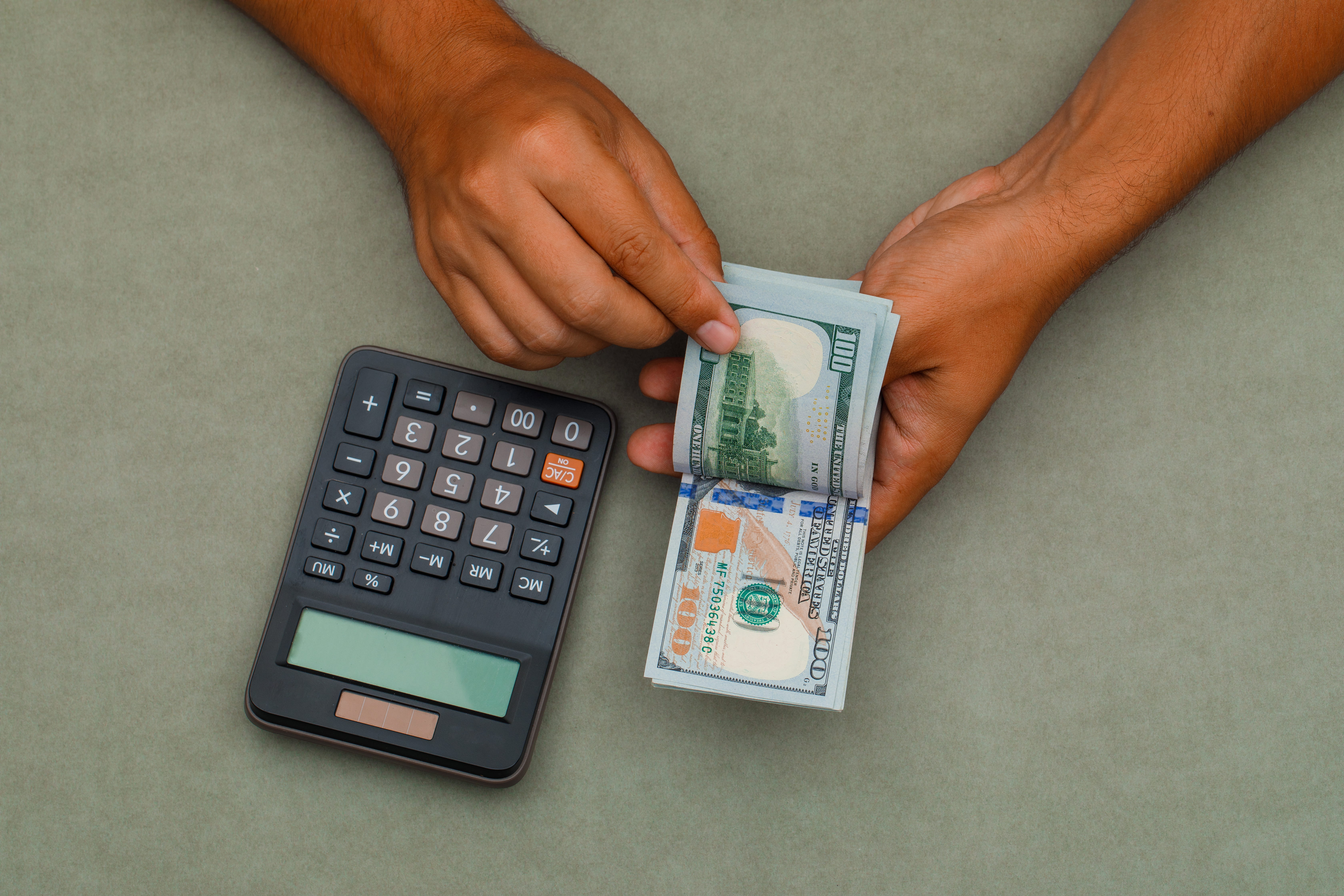 Hands counting US hundred-dollar notes beside a calculator